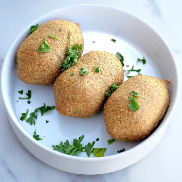 Three golden-brown kibbeh, garnished with fresh parsley, served in a white bowl.