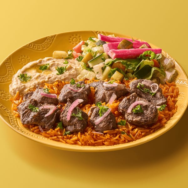 Plate of meat chunks over orange rice, with hummus, salad, and pink pickled vegetables.