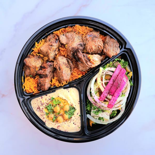 Overhead view of a Don Kabob meal with rice, meat, hummus, and salad in a black to-go container.